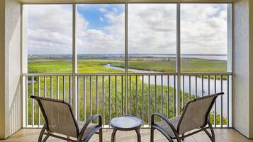 Un balcon avec deux chaises et une petite table, donnant sur une rivière et un paysage verdoyant.