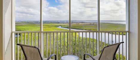A balcony with two chairs and a small table, overlooking a river and green landscape.