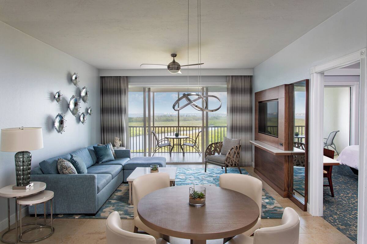Uma sala de estar moderna com sofá, mesa de centro, cadeiras, uma varanda com vista e uma televisão.
