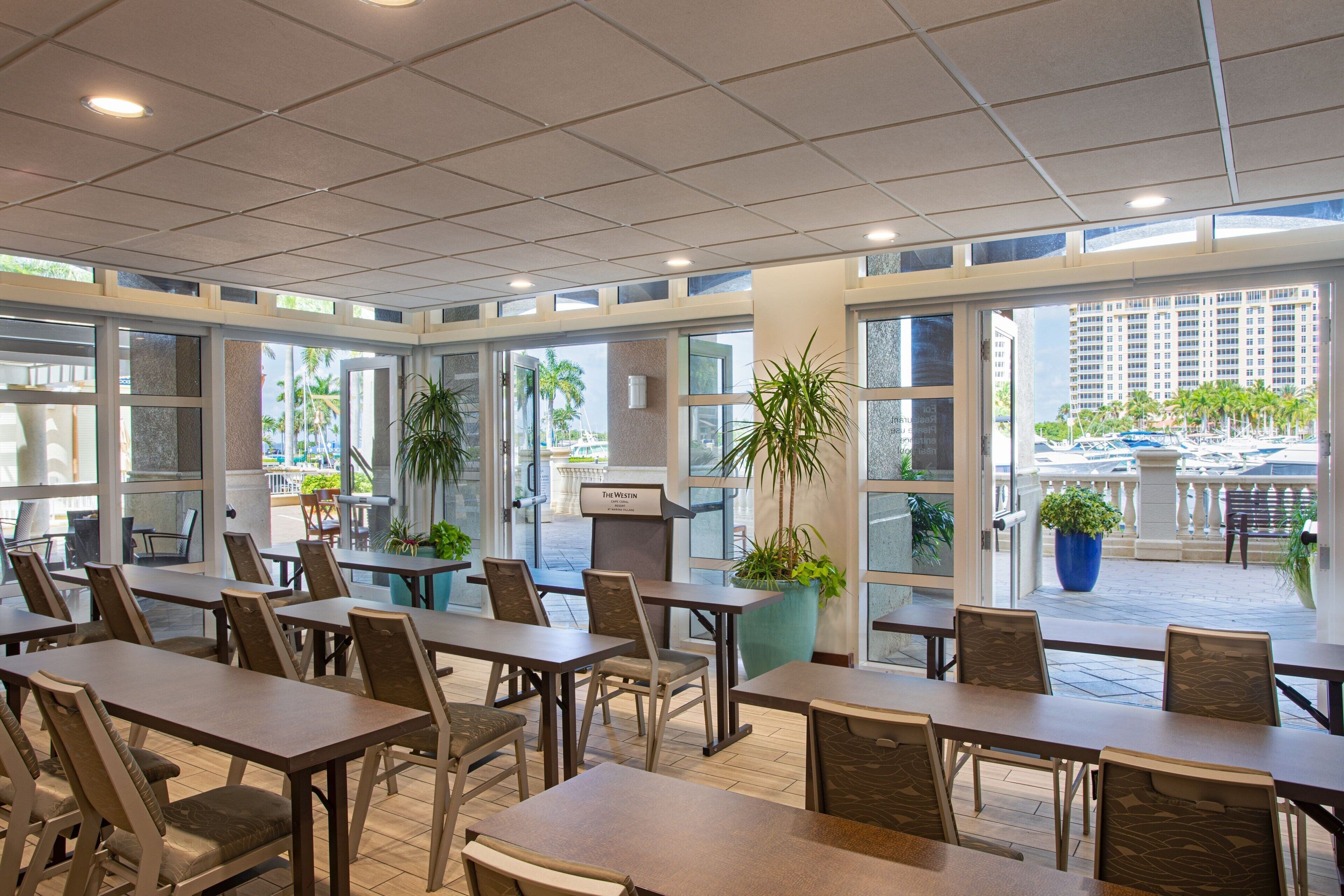 Un amplio comedor interior con varias mesas y sillas, ventanas grandes y plantas en macetas.