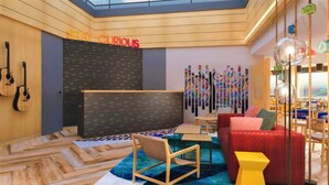 A modern interior with a wooden floor, a black wall with a 'STAY CURIOUS' sign, a colorful abstract art piece, and a red sofa. - Ginger Bangalore Whitefield (Bengaluru)