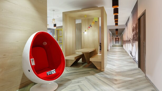 Un pasillo moderno con una butaca roja en forma de huevo, escalones de madera y un suelo con diseño de espiga.