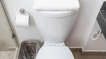 A white toilet with a sign above it, a plastic trash bin, and a toilet paper holder on the wall.