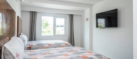 A hotel room with two beds, a flat-screen TV, an air conditioning unit, and a window with curtains.