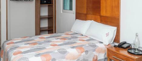 A bedroom with a bed, a bedside table, a wardrobe, and a wooden headboard.