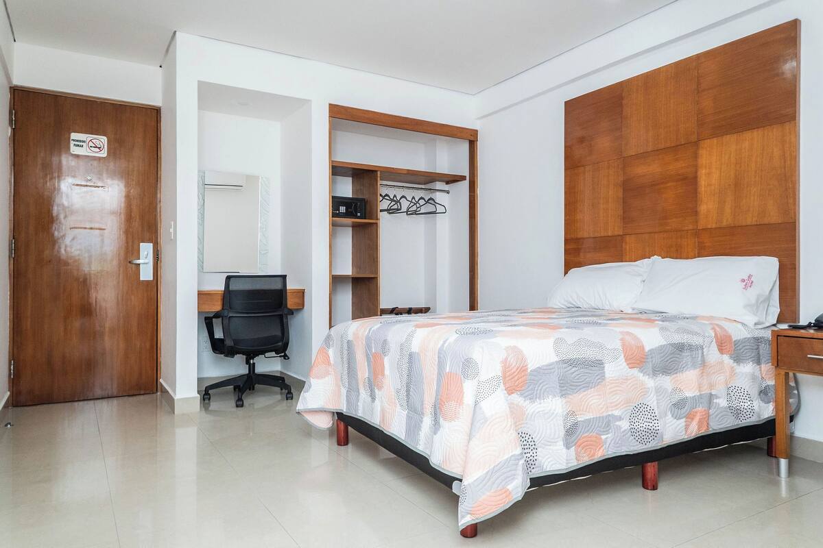 A bedroom with a bed, a wooden headboard, a wardrobe, and a desk with a chair.