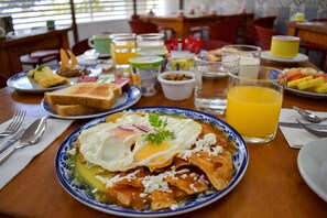 Una mesa de desayuno con platos de comida, un vaso de jugo de naranja y diferentes aderezos.