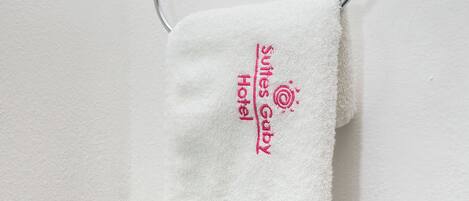Une serviette blanche est suspendue à un porte-serviettes en métal, orné d’un logo et d’une inscription indiquant qu’elle provient de l’hôtel Sultes Gaby.