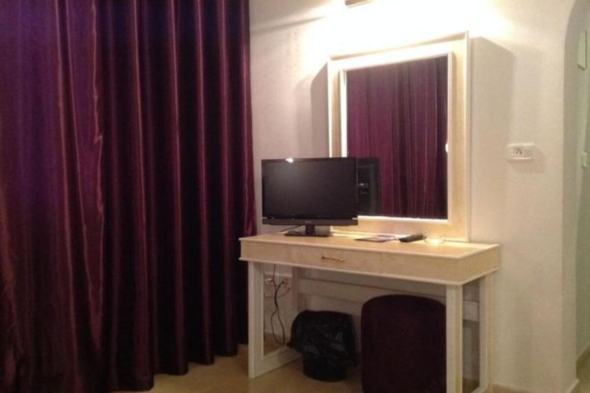 A room with a desk, a flat-screen TV, a mirror, and a dark chair.