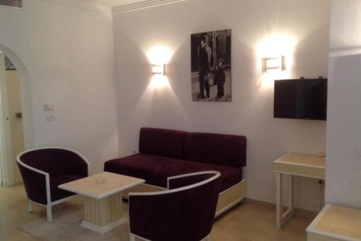 A modern room with a dark red sofa, two white armchairs, a small table, and a flat-screen TV mounted on the wall.