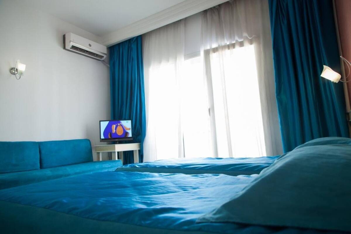 Una habitación de hotel con una cama, un televisor sobre una mesita y una ventana con cortinas.