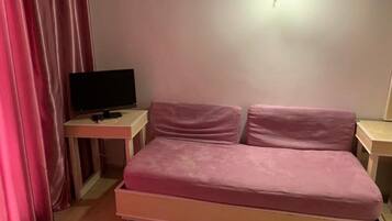 A bedroom with a bed, a desk with a computer, and a wall-mounted light.