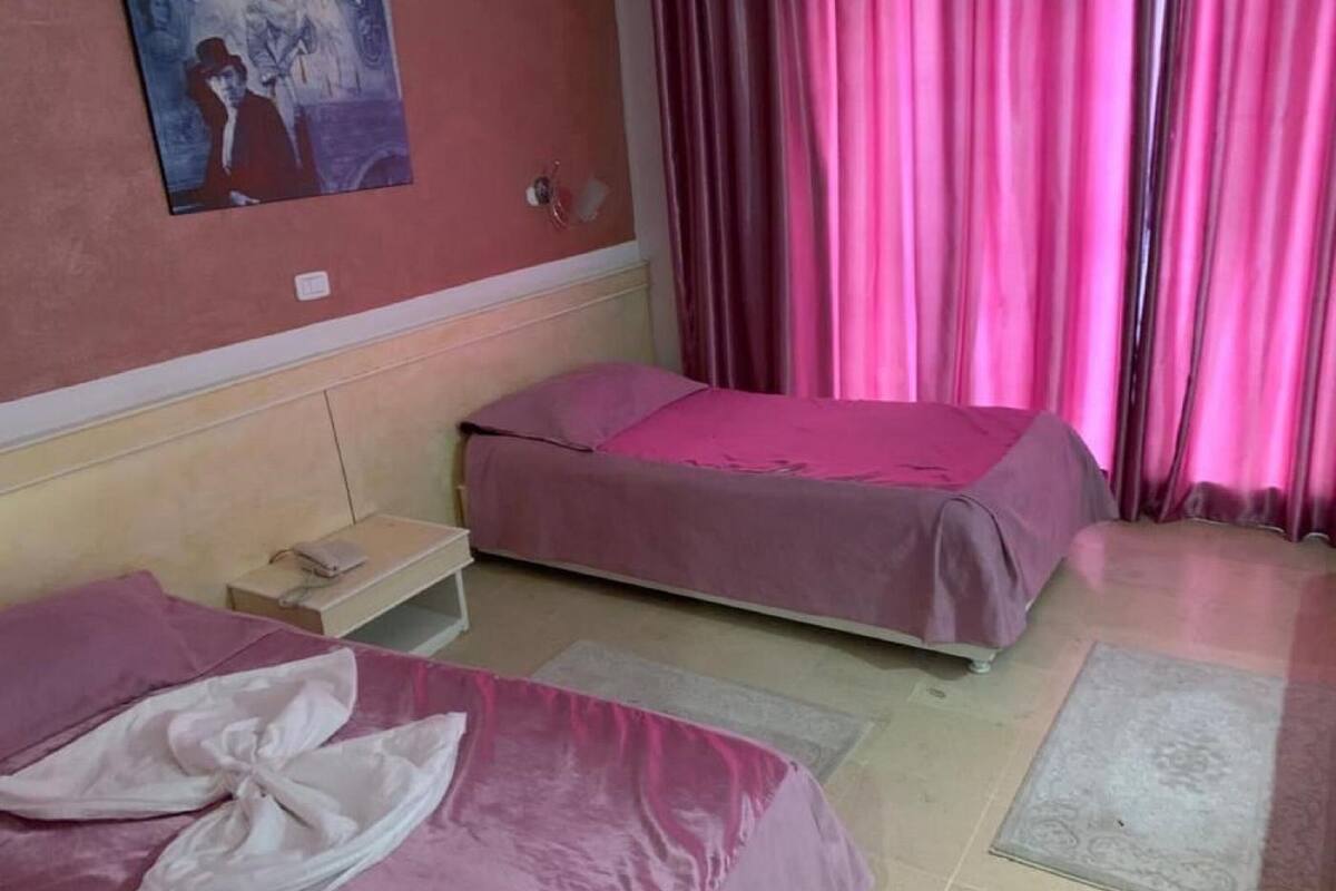 Una habitación de hotel con dos camas, una mesita de noche, un teléfono en la pared y un cuadro.