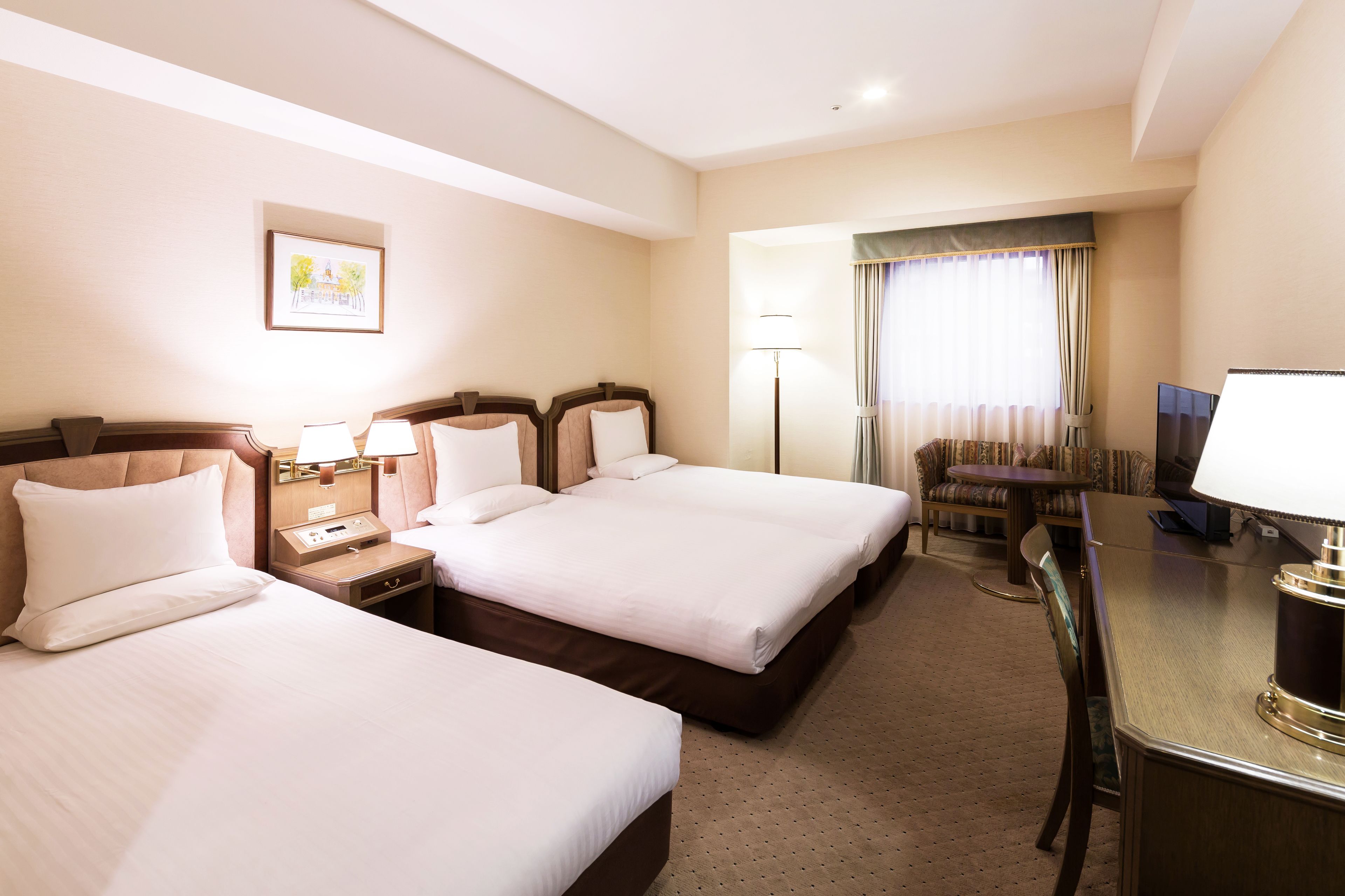 A hotel room with two beds, a desk, a chair, a lamp, and a TV.