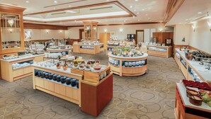 A hotel dining area with multiple buffet stations, wooden furniture, and a patterned carpet. - Hotel Mystays Sapporo Aspen (Sapporo)