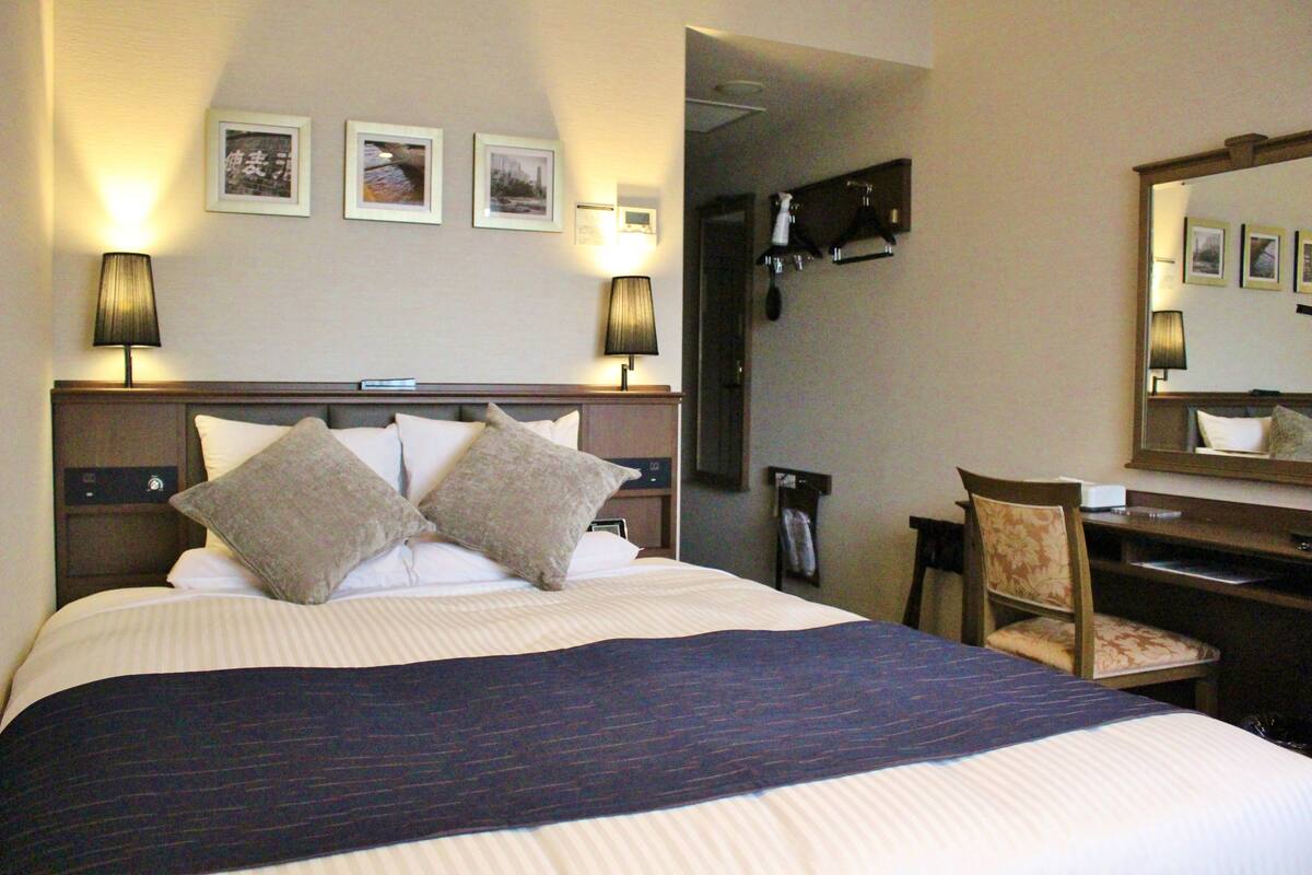 Ein Hotelzimmer mit einem großen Bett, zwei Nachttischlampen, einem Schreibtisch mit Stuhl und einem Spiegel an der Wand.