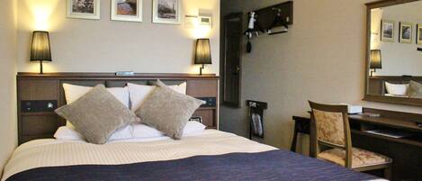 A hotel room with a large bed, two bedside lamps, a desk with a chair, and a mirror on the wall.