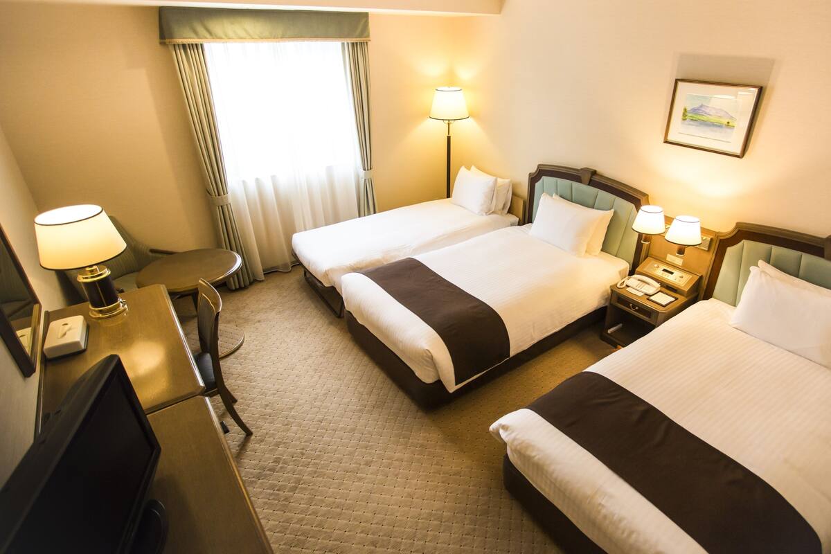 Ein Hotelzimmer mit zwei Betten, einem Schreibtisch, einem Stuhl, einer Lampe und einem gerahmten Bild an der Wand.