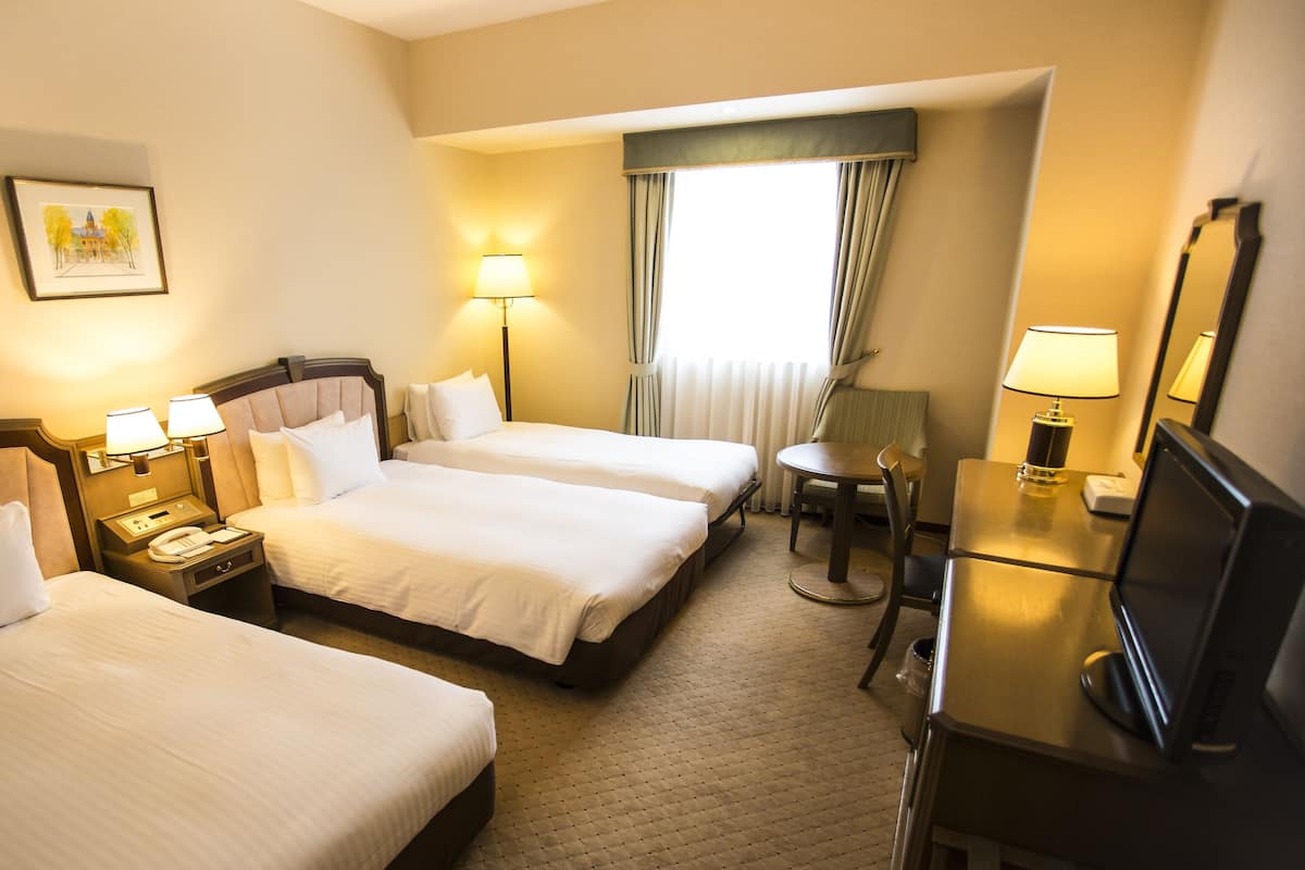 Ein Hotelzimmer mit zwei Betten, einem Schreibtisch mit Stuhl, einer Lampe und einem Fernseher.