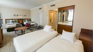 A hotel room with two beds, a sitting area with chairs, a desk, a mirror, and a bathroom with a sink and mirror. - Hotel Mystays Sapporo Aspen (Sapporo)