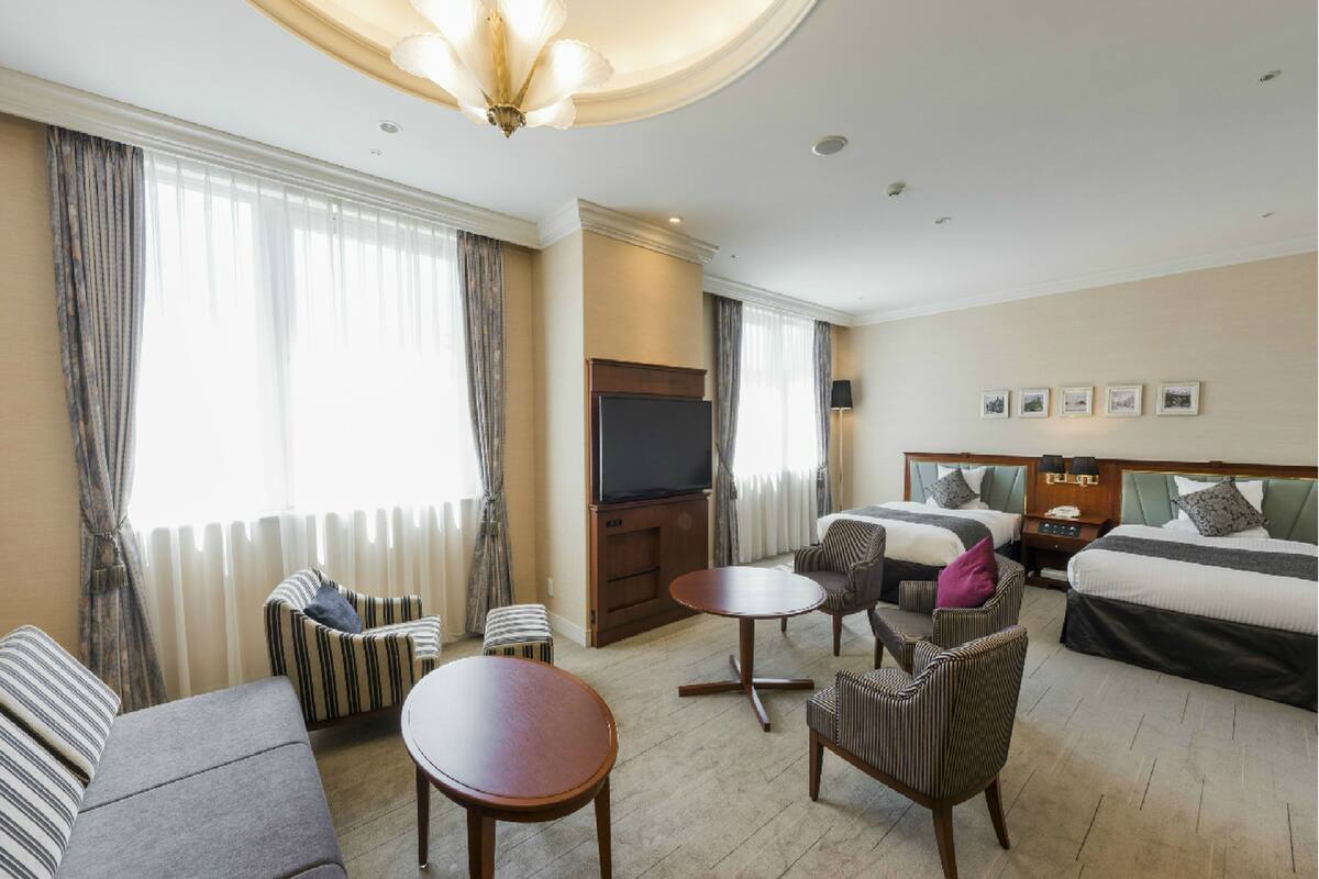 Ein Hotelzimmer mit Sofa, Sessel, rundem Tisch und einem Bett mit Kopfteil.