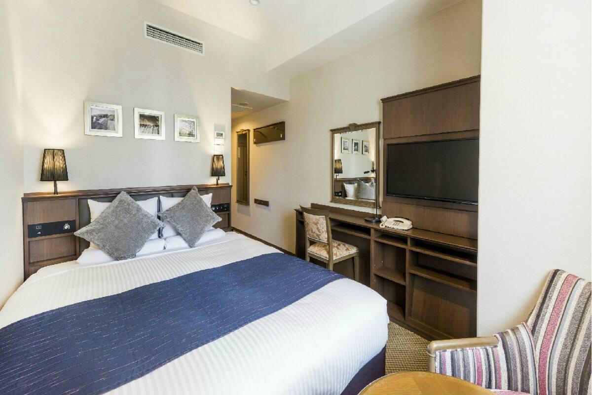 Ein Hotelzimmer mit einem großen Bett, einem Schreibtisch mit Stuhl, einem Fernseher und einem Spiegel.