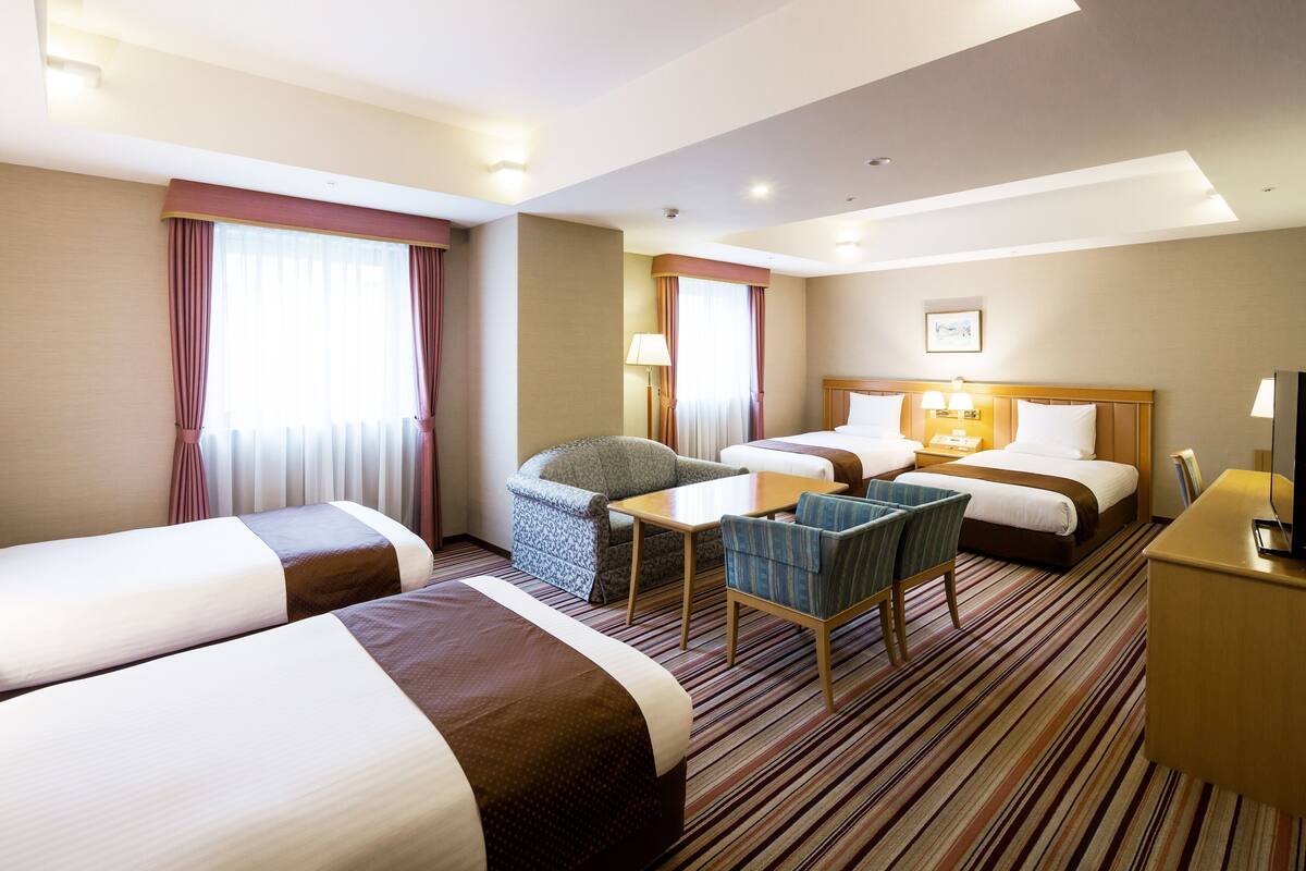 Ein Hotelzimmer mit zwei Betten, einem Schreibtisch, einem Stuhl und einem Fernseher.