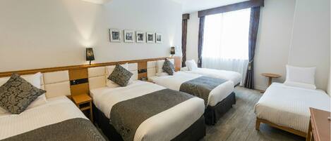 Habitación de hotel con tres camas, un escritorio pequeño y una ventana con cortinas.