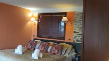 Una habitación de hotel con una cama, dos lámparas fijadas a la pared, una ventana con persianas y una pequeña mesa con lámpara.