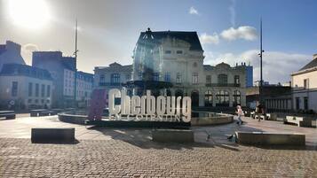 A cobblestone plaza with a fountain and a large sign reading "Cherbourg".