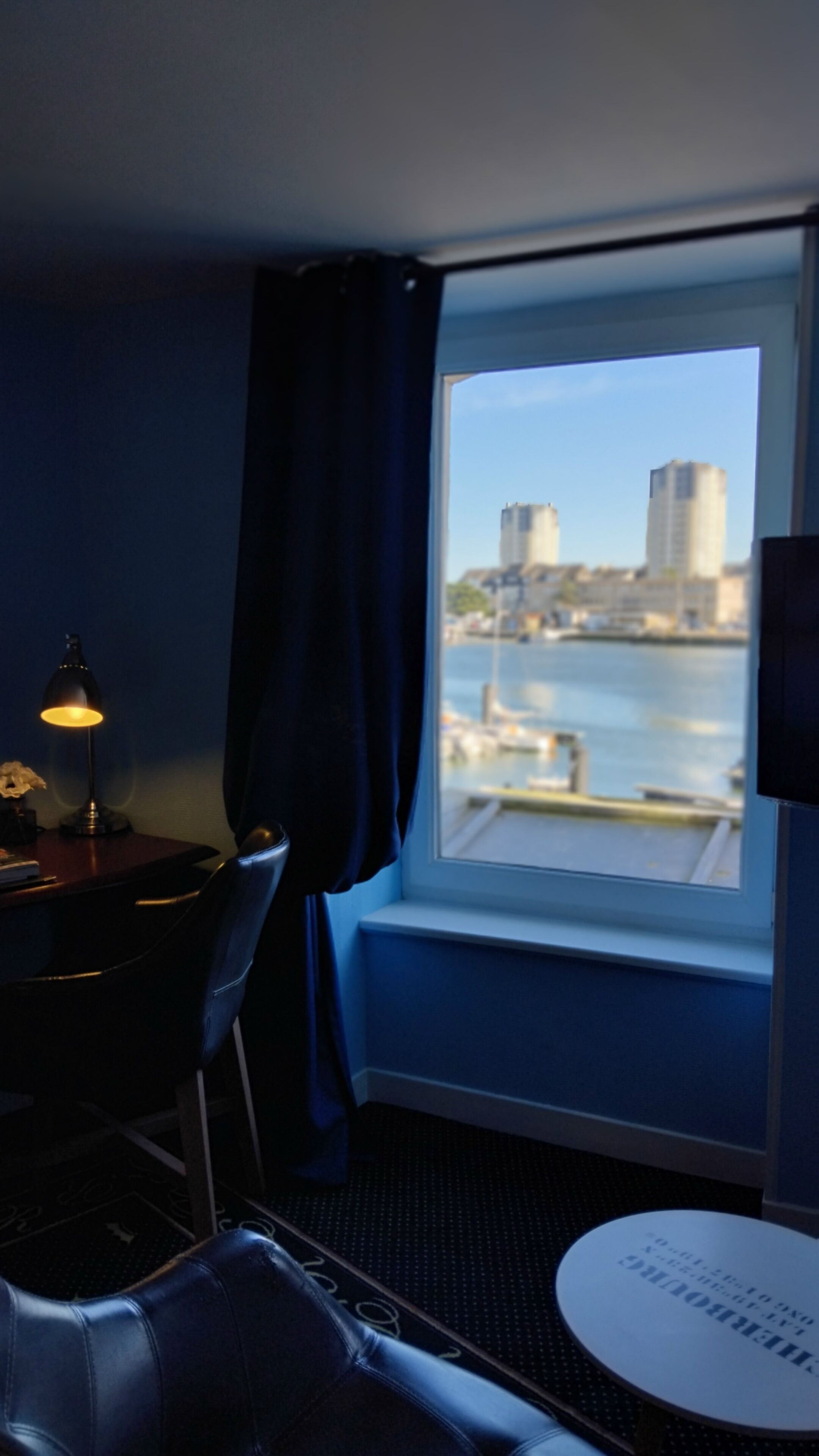 A hotel room with a view of a marina and buildings across the water.