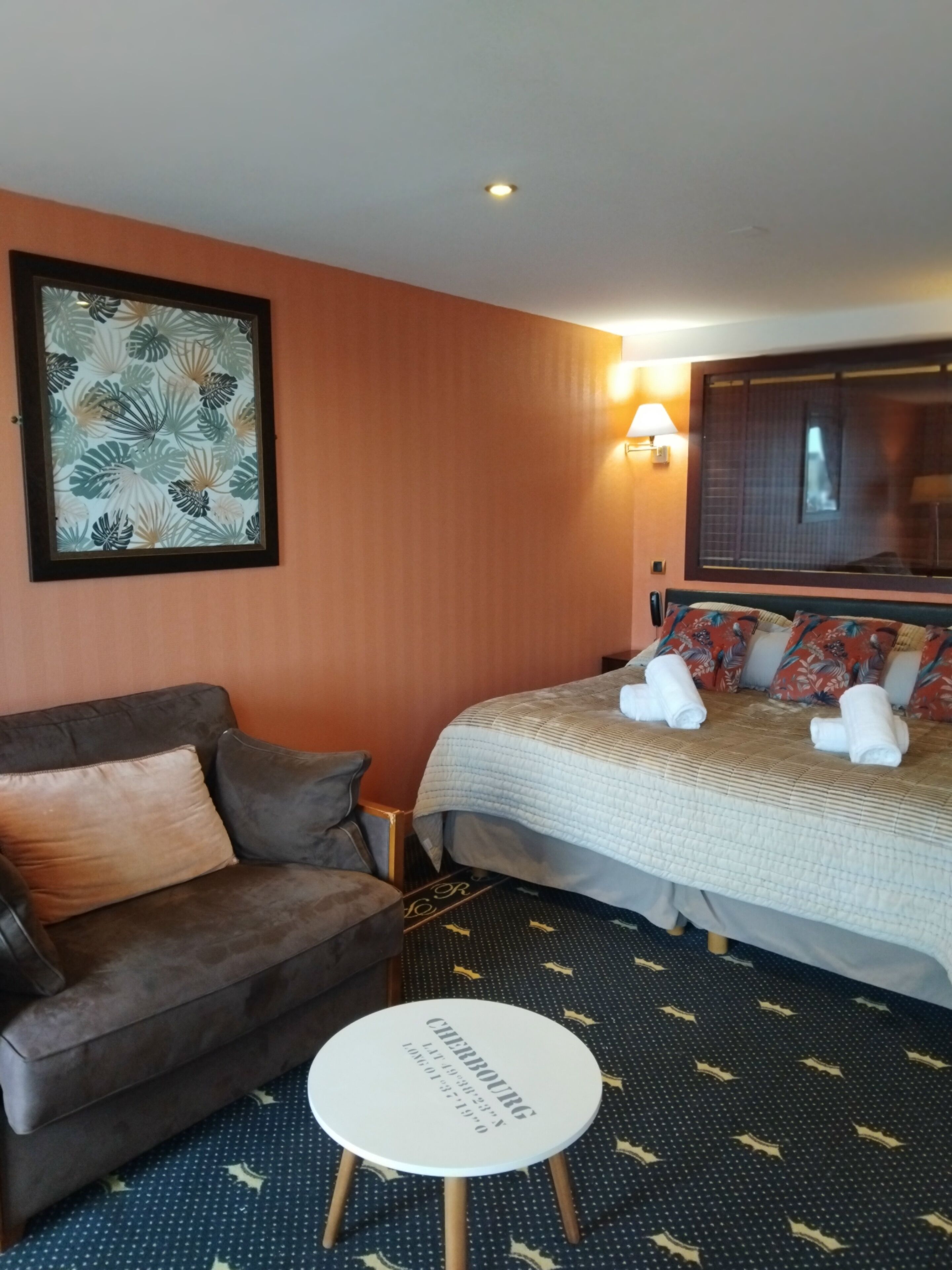 Habitación de hotel con cama, sofá, una mesita y televisor instalado en la pared.