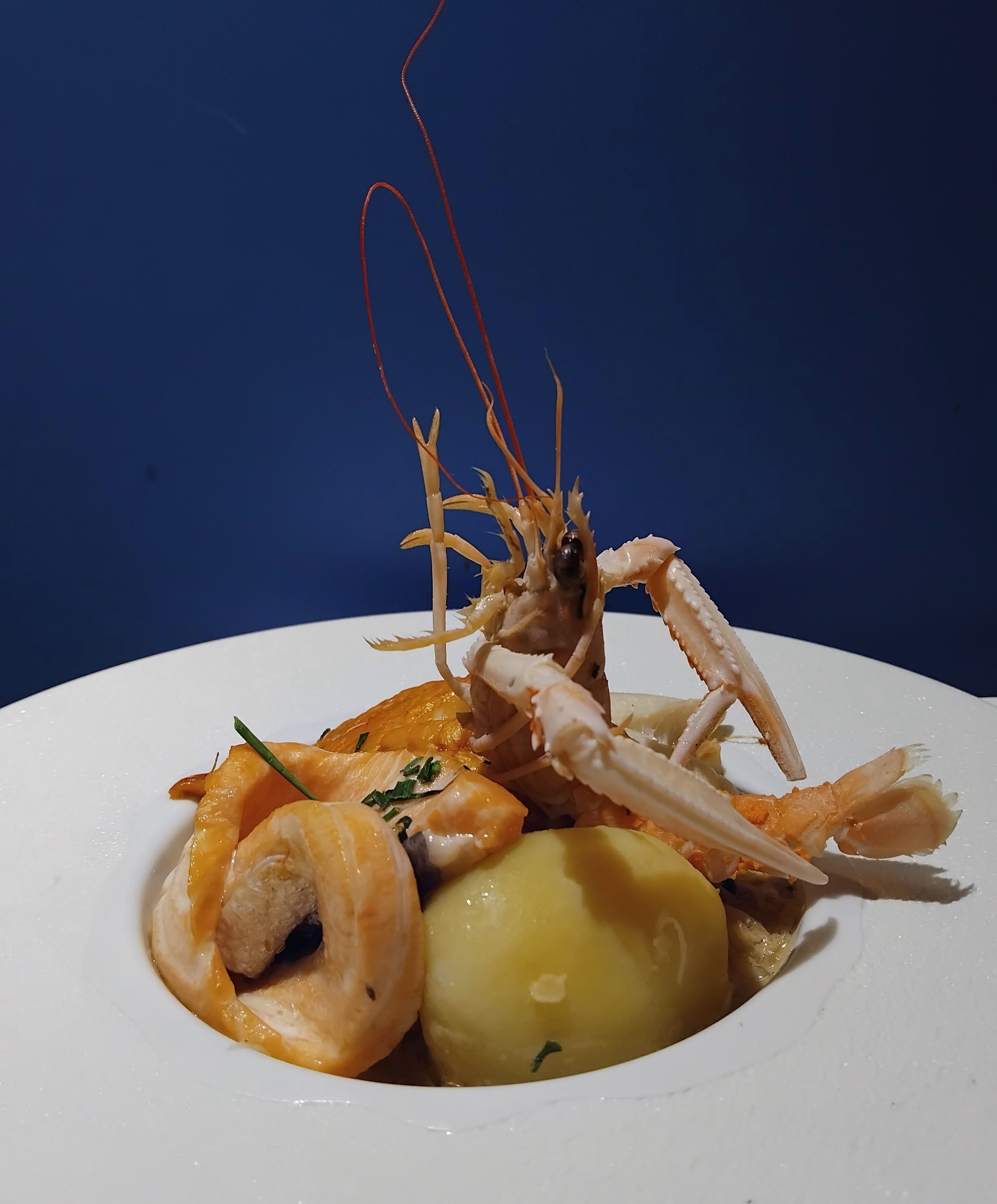 Een visgerecht met garnalen, zalm en aardappelen op een wit bord.