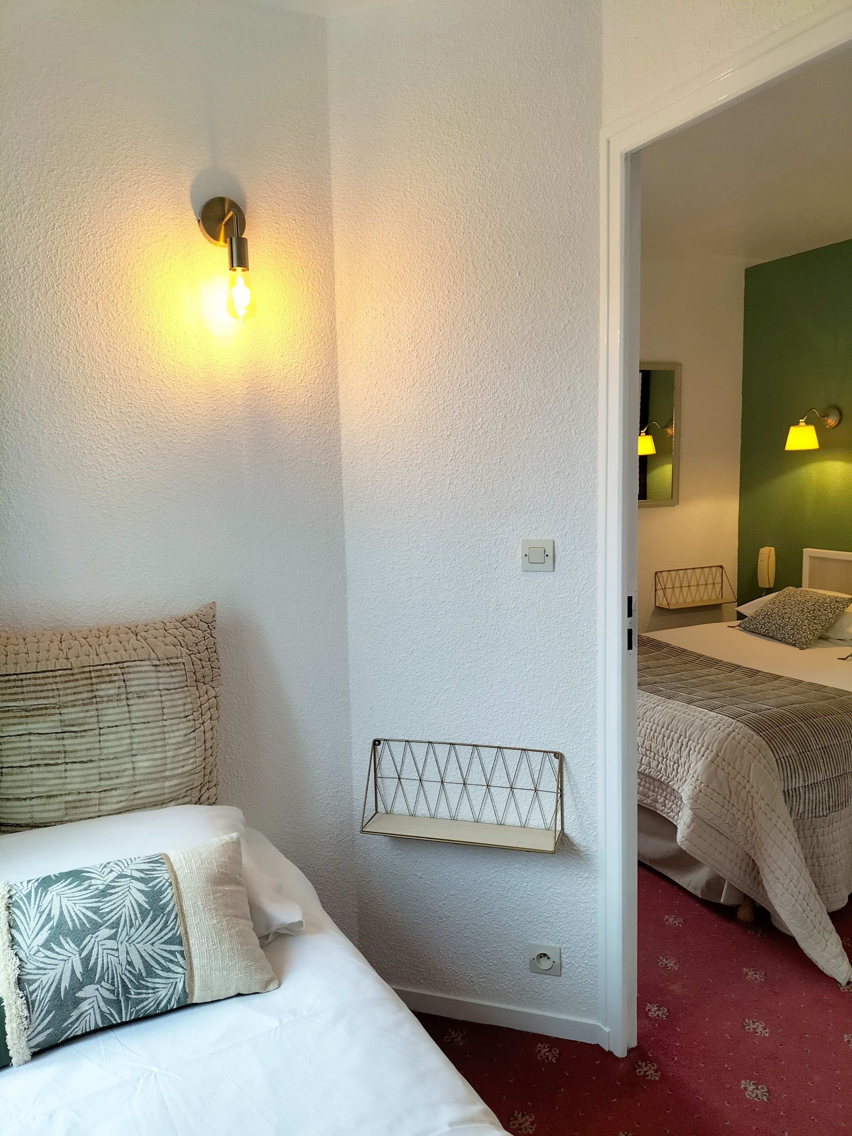 Ett hotellrum med en säng, ett sängbord, en hylla på väggen och en spegel.