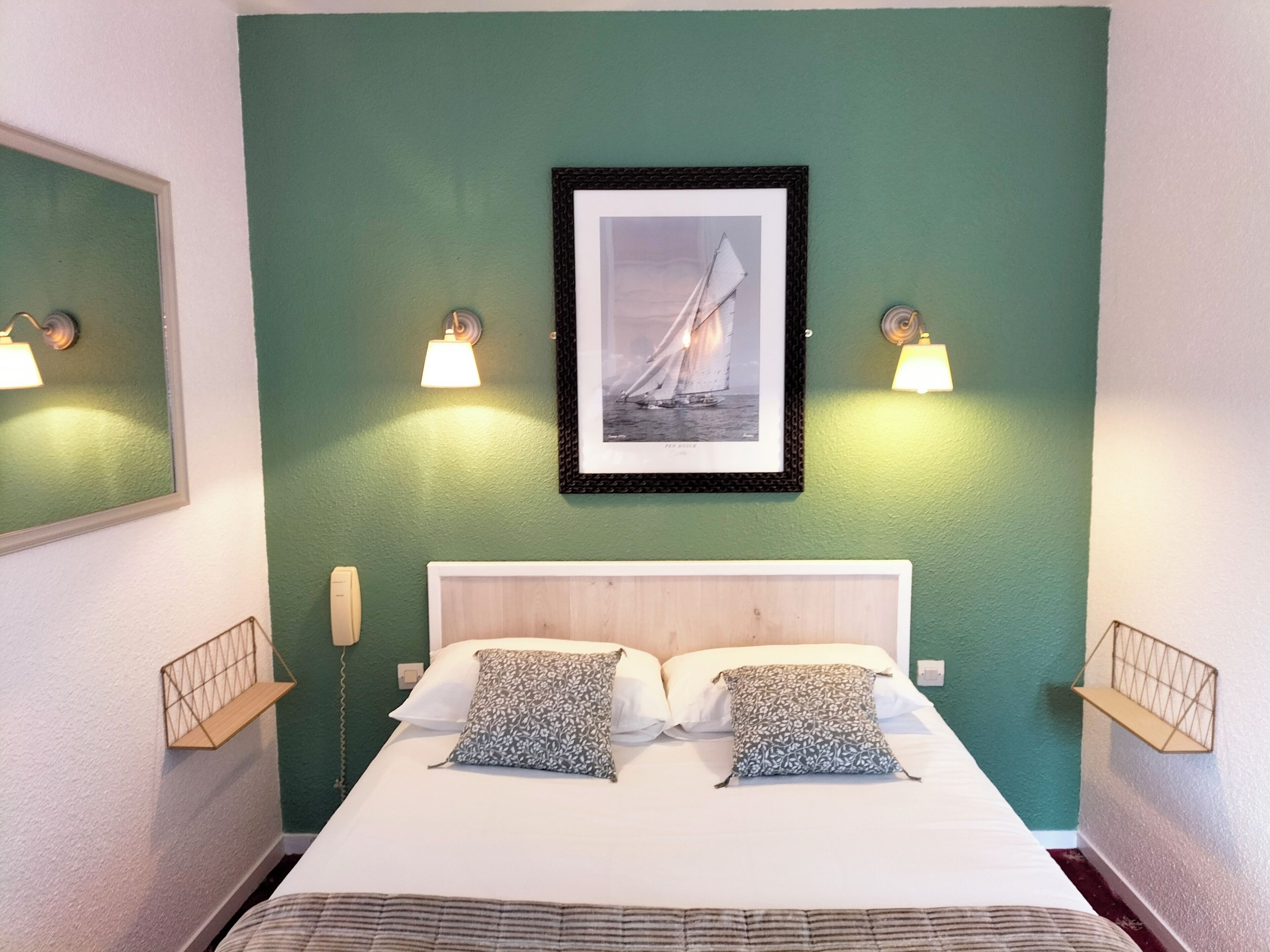 A neatly arranged bedroom with a bed, two pillows, a framed picture on the wall, and two wall-mounted lamps.