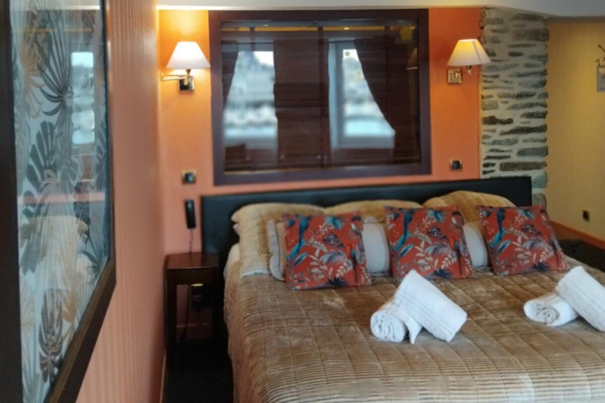 Une chambre d’hôtel avec un lit, deux lampes de chevet, une fenêtre et un mur orné d’un miroir décoratif.