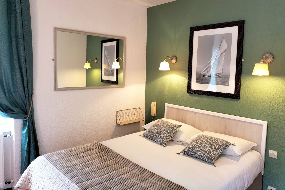 Una habitación de hotel con una cama, dos lámparas de pared, un cuadro enmarcado y un teléfono.
