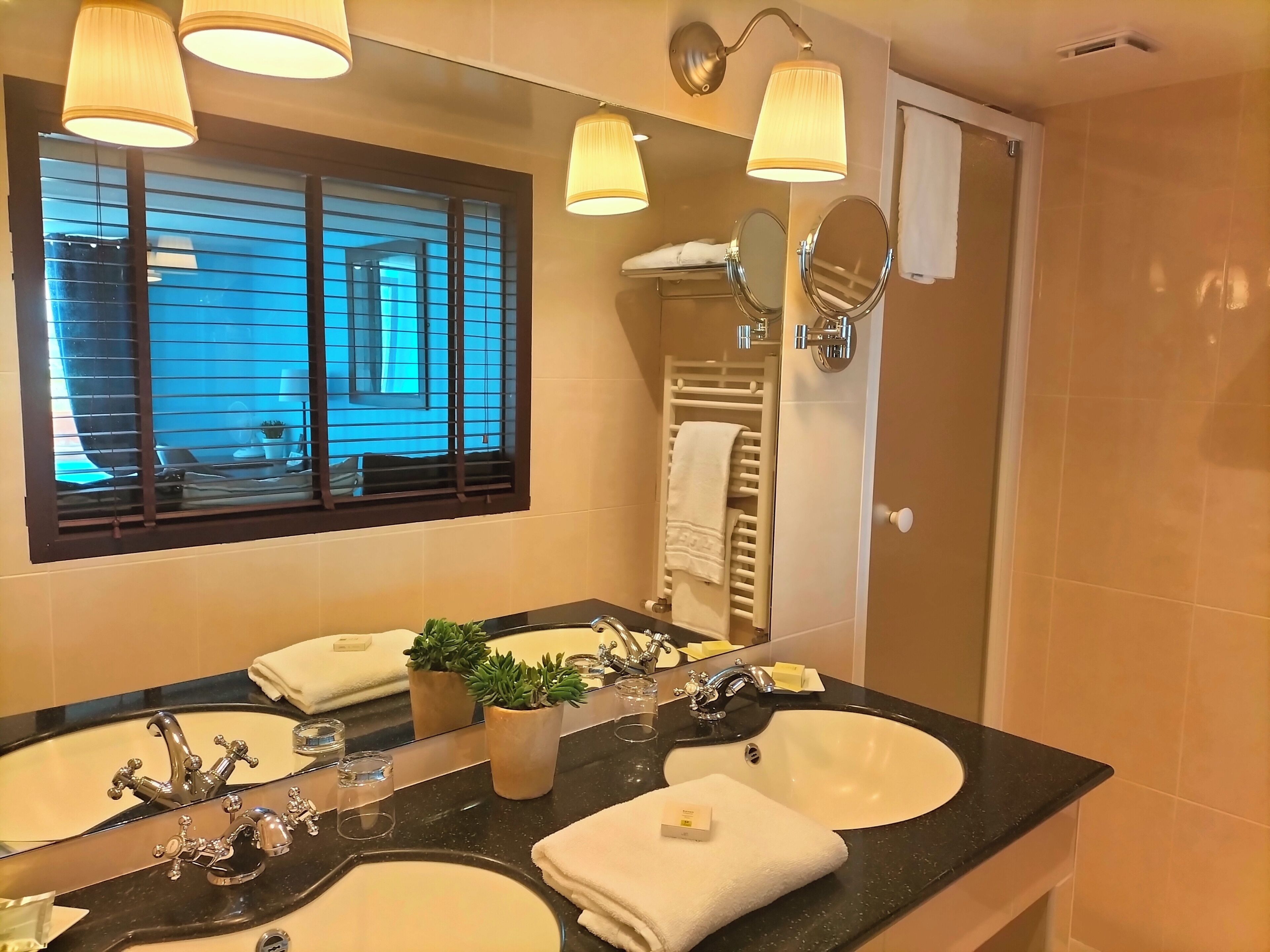 A bathroom with two sinks, a large mirror, and a window with blinds.