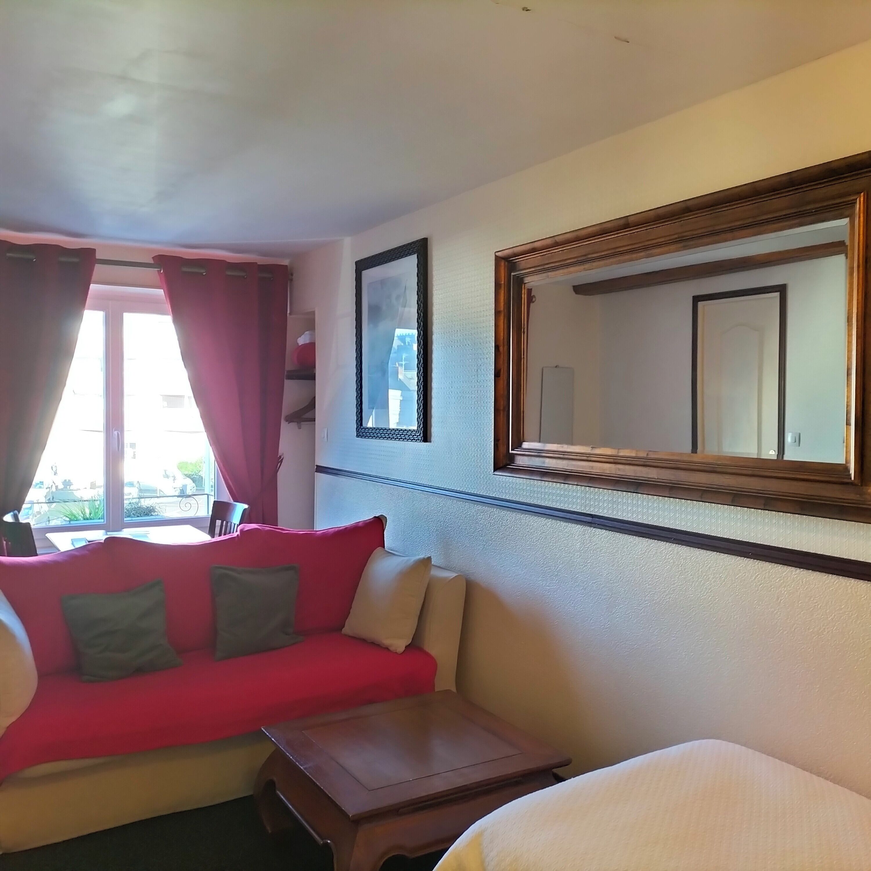 A hotel room with a red sofa, a small wooden table, and a large mirror on the wall.