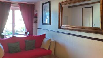 A hotel room with a red sofa, a small wooden table, and a large mirror on the wall.