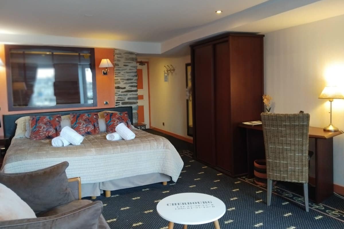 Una habitación de hotel con cama, una silla, una mesita y un armario.