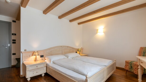 A bedroom with a wooden bed, two bedside tables with lamps, a chair, and a wall-mounted light fixture. - DA ELDA natural retreat (Ledro)