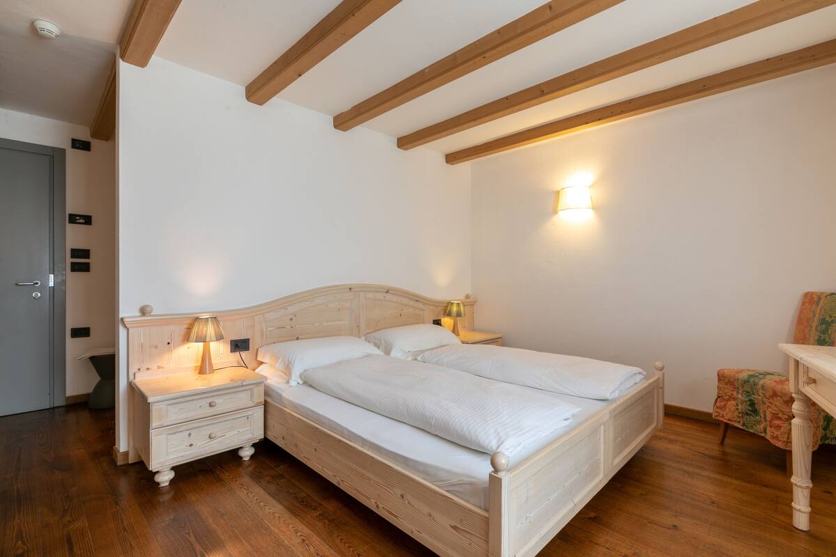 Un dormitorio con una cama de madera, dos mesitas de noche con lámparas, una silla y un aplique de pared.