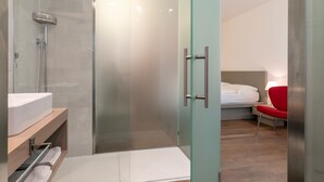 A modern bathroom with a glass shower enclosure, a white sink, and a red chair. - DA ELDA natural retreat (Ledro)