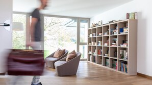 A modern living room with a large bookshelf, a sofa, and a large window. - DA ELDA natural retreat (Ledro)