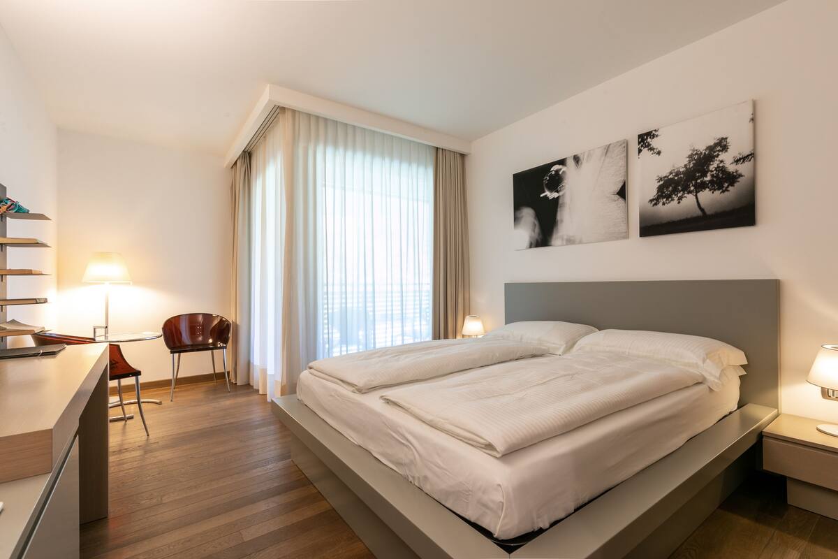 Una habitación de hotel moderna con cama, mesitas de noche, escritorio y una silla.