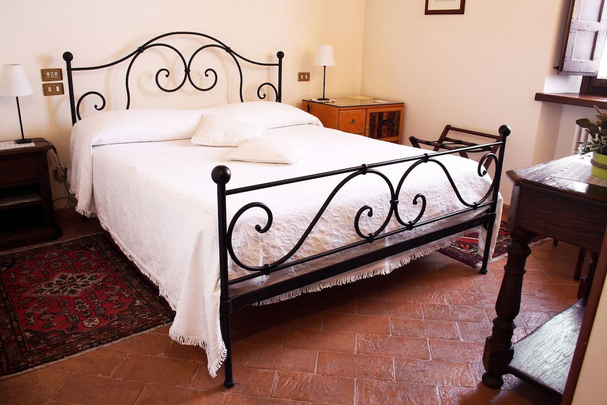 A bed with a metal frame, a nightstand, a lamp, a small wooden cabinet, and a chair.