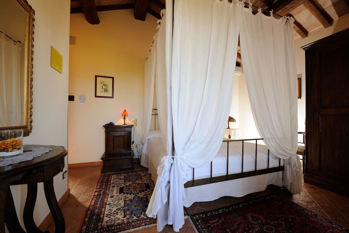 A bedroom with a bed, a nightstand, a lamp, a mirror, and a window with curtains.