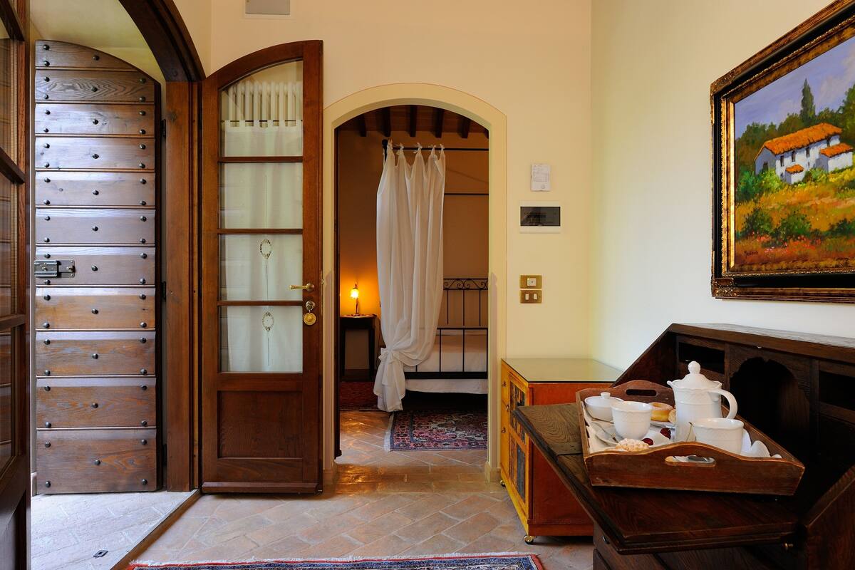 A room with a wooden cabinet, a bed with a white curtain, a painting on the wall, and a tray with kitchen items.