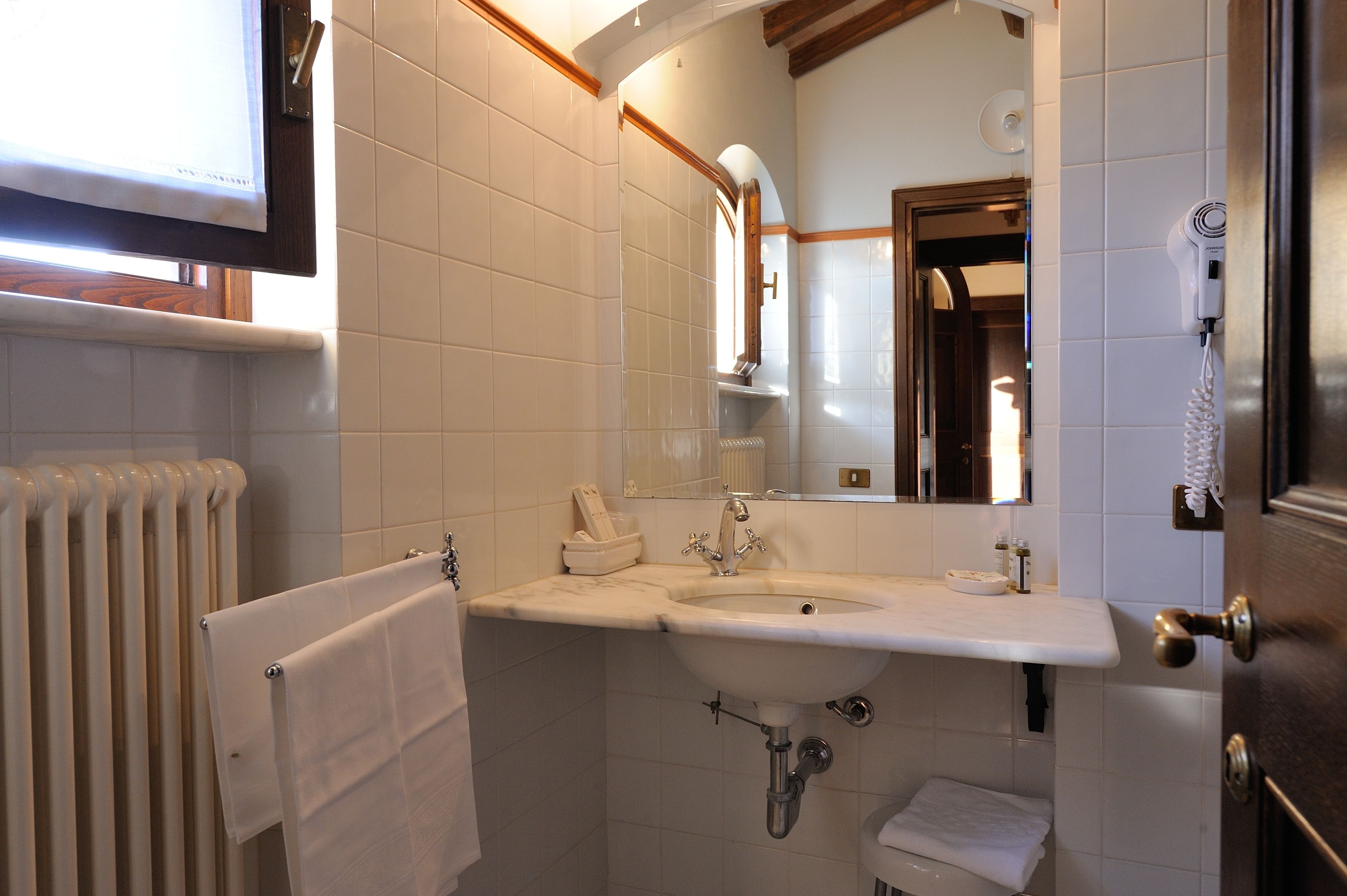 Un baño con lavamanos blanco, espejo y toallero.
